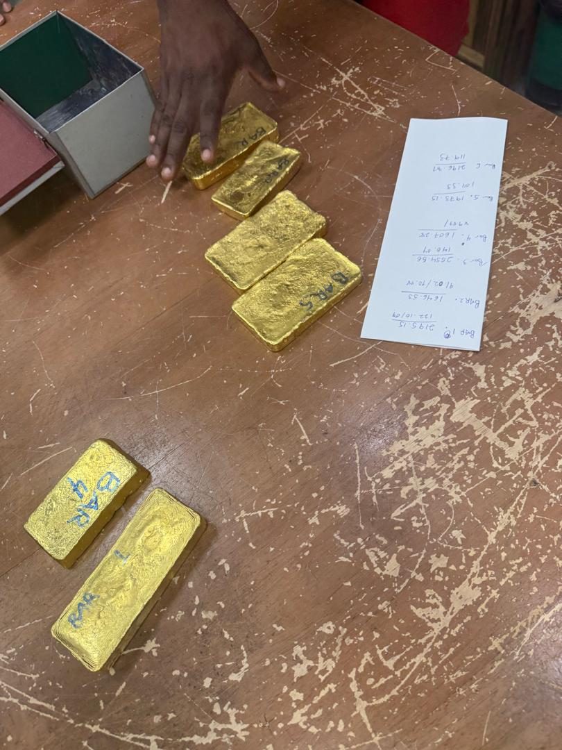 Six numbered gold bars laid out on a table beside a handwritten weighing and valuation tally sheet